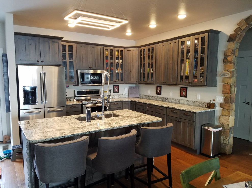 Example of a mid-sized transitional l-shaped medium tone wood floor and brown floor eat-in kitchen design with an undermount sink, shaker cabinets, gray cabinets, granite countertops, stainless steel appliances, an island and multicolored countertops