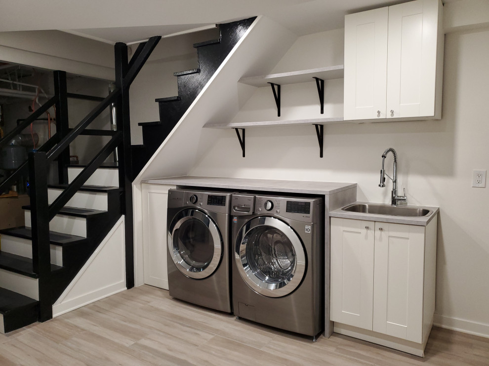 This is an example of a contemporary single-wall utility room in DC Metro with a single-bowl sink, shaker cabinets, grey cabinets, concrete benchtops, white walls, laminate floors, a side-by-side washer and dryer, grey floor and grey benchtop.