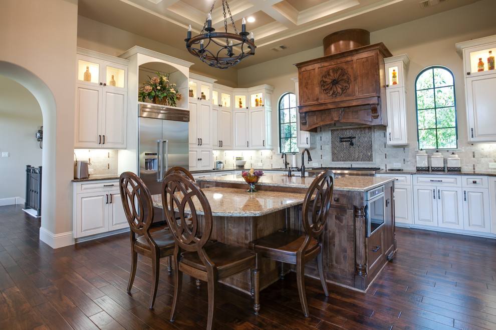Photo of an expansive traditional l-shaped open plan kitchen in Dallas with a farmhouse sink, louvered cabinets, white cabinets, granite benchtops, white splashback, cement tile splashback, stainless steel appliances, dark hardwood floors, multiple islands and brown floor.