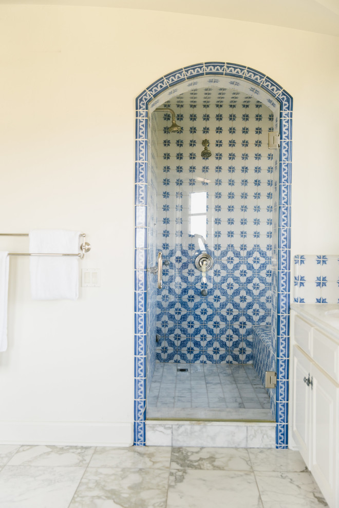 Design ideas for a large mediterranean master bathroom in Los Angeles with raised-panel cabinets, white cabinets, an alcove tub, an alcove shower, a one-piece toilet, blue tile, ceramic tile, white walls, marble floors, a drop-in sink, granite benchtops, white floor, a hinged shower door and white benchtops.