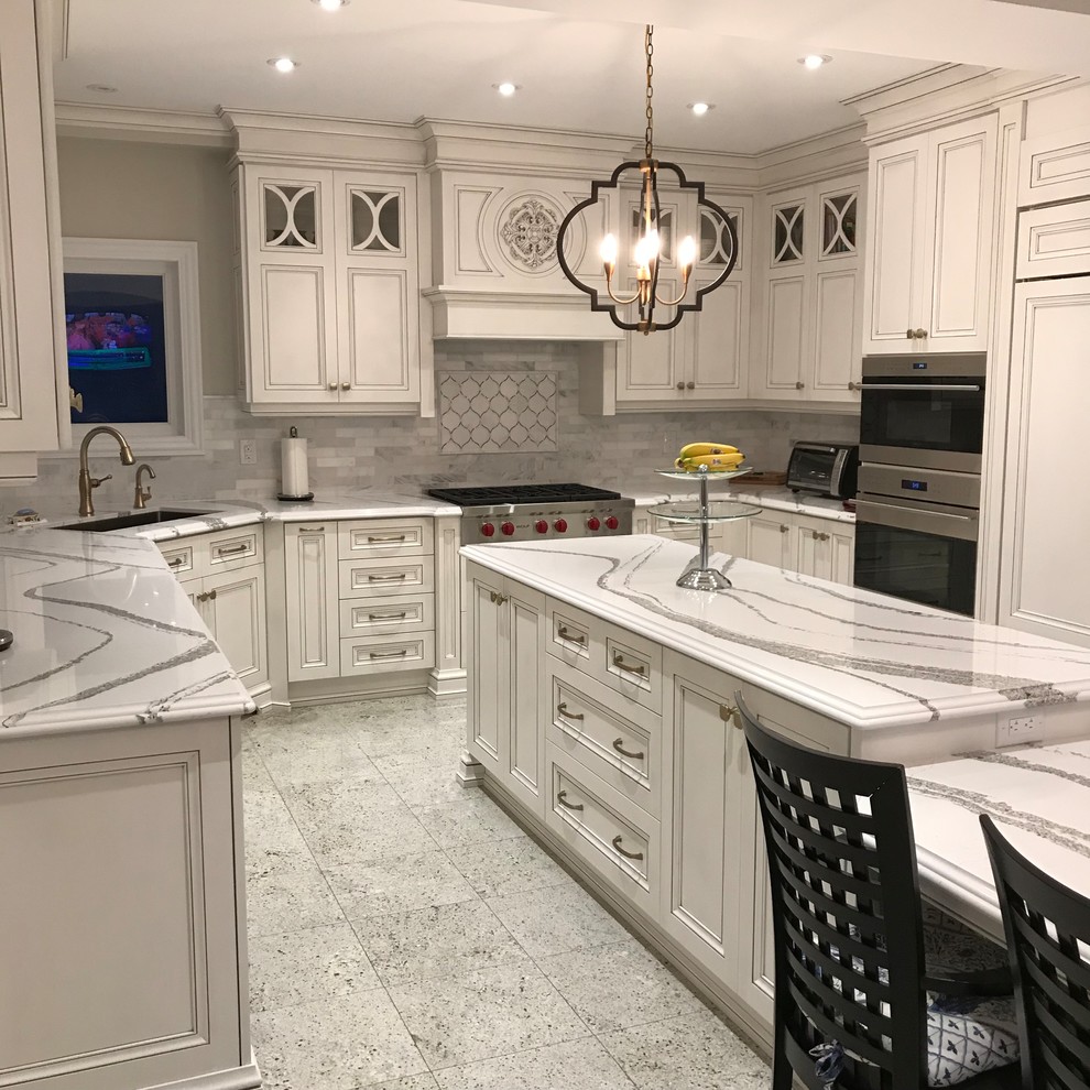 Expansive traditional u-shaped eat-in kitchen in Toronto with an undermount sink, recessed-panel cabinets, distressed cabinets, quartz benchtops, white splashback, marble splashback, panelled appliances, with island, white floor and white benchtop.