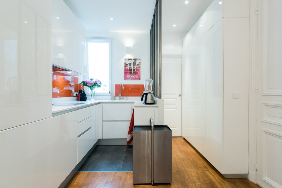 Photo of a mid-sized modern u-shaped open plan kitchen in Paris with an integrated sink, beaded inset cabinets, white cabinets, quartzite benchtops, orange splashback, glass tile splashback, panelled appliances and terra-cotta floors.