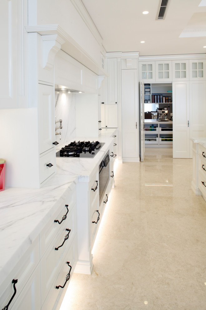 Photo of a traditional l-shaped kitchen in Sydney with a farmhouse sink, recessed-panel cabinets, white cabinets, marble benchtops, white splashback, marble splashback, black appliances, marble floors, beige floor and white benchtop.