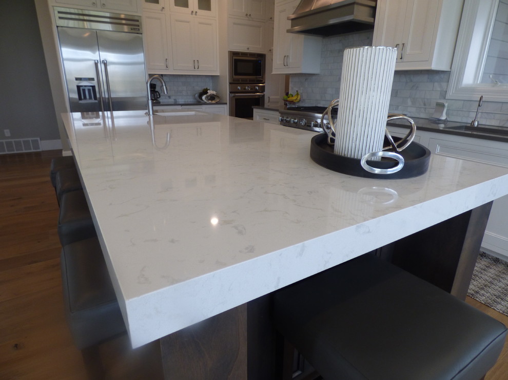 Large transitional l-shaped light wood floor eat-in kitchen photo with an undermount sink, recessed-panel cabinets, white cabinets, quartz countertops, white backsplash, subway tile backsplash, stainless steel appliances and an island