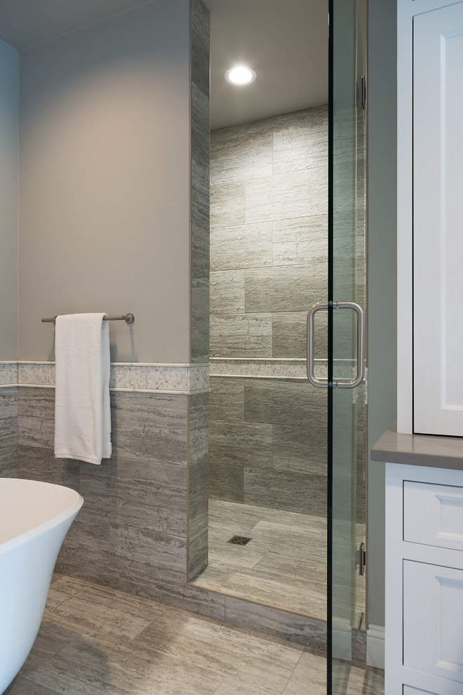 Inspiration for a large transitional gray tile and porcelain tile marble floor freestanding bathtub remodel with recessed-panel cabinets, gray walls, a vessel sink, solid surface countertops and white cabinets