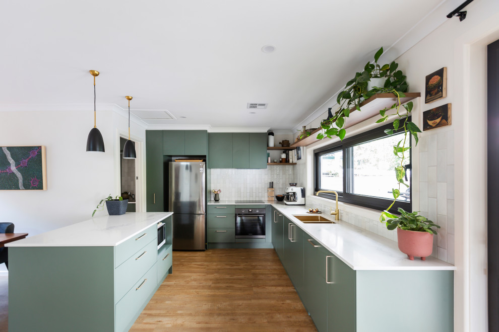 This is an example of a mid-sized eclectic u-shaped open plan kitchen in Canberra - Queanbeyan with an undermount sink, flat-panel cabinets, green cabinets, quartz benchtops, grey splashback, ceramic splashback, stainless steel appliances, medium hardwood floors, with island, brown floor and white benchtop.