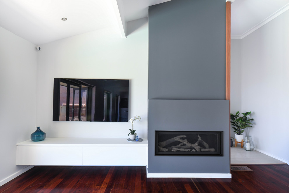 This is an example of a medium sized modern open plan living room in Sydney with dark hardwood flooring, a plastered fireplace surround, a wall mounted tv, brown floors, exposed beams and multi-coloured walls.