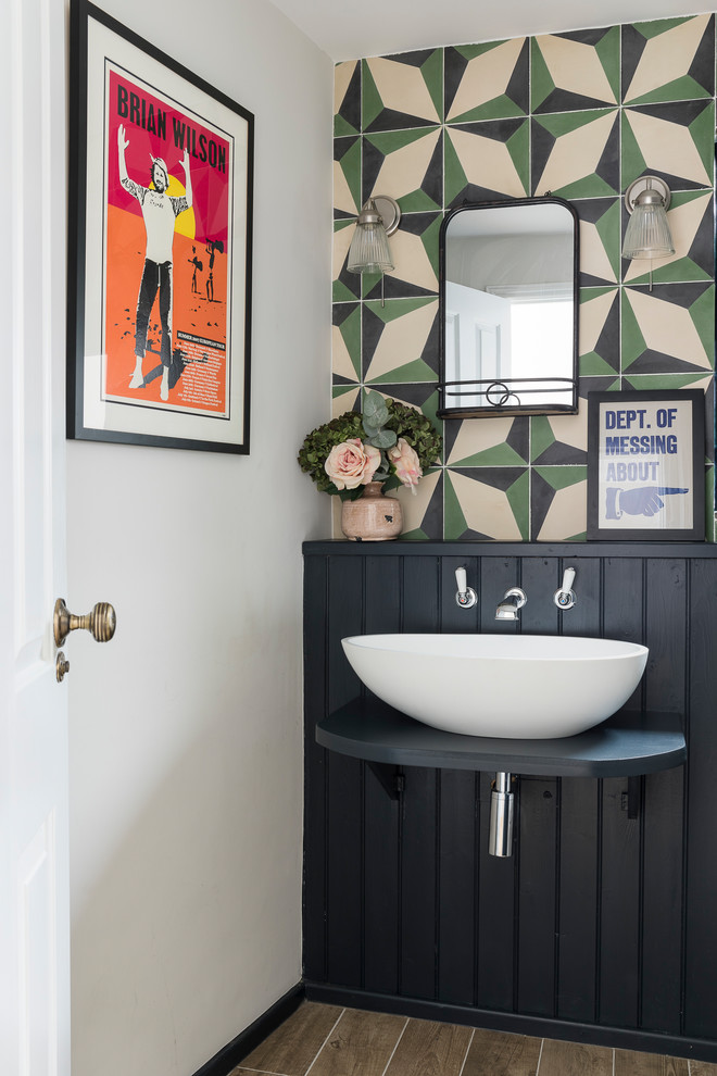 Eclectic powder room in Hertfordshire with multi-coloured walls, a vessel sink, brown floor and black benchtops.