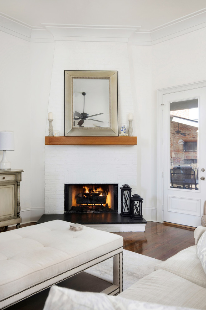 Inspiration for a mid-sized transitional enclosed living room in New Orleans with white walls, dark hardwood floors, a corner fireplace, a brick fireplace surround, no tv, brown floor and exposed beam.