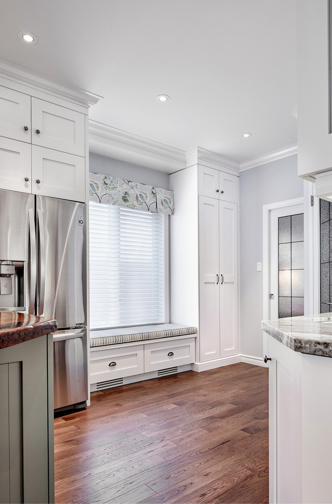 Large transitional medium tone wood floor home design photo in Toronto with a farmhouse sink, shaker cabinets, white cabinets, granite countertops, white backsplash, subway tile backsplash, stainless steel appliances and an island
