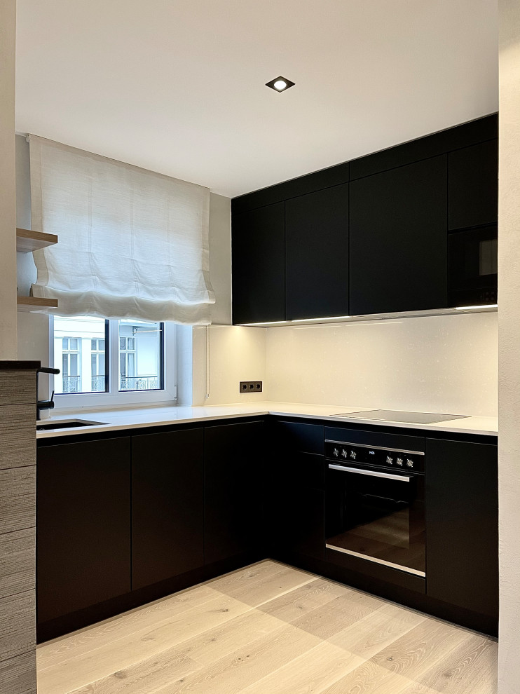Küche ohne Insel in L-Form mit Unterbauwaschbecken, flächenbündigen Schrankfronten, schwarzen Schränken, Quarzwerkstein-Arbeitsplatte, Küchenrückwand in Beige, Rückwand aus Quarzwerkstein, Küchengeräten aus Edelstahl, hellem Holzboden, beigem Boden und beiger Arbeitsplatte in Berlin