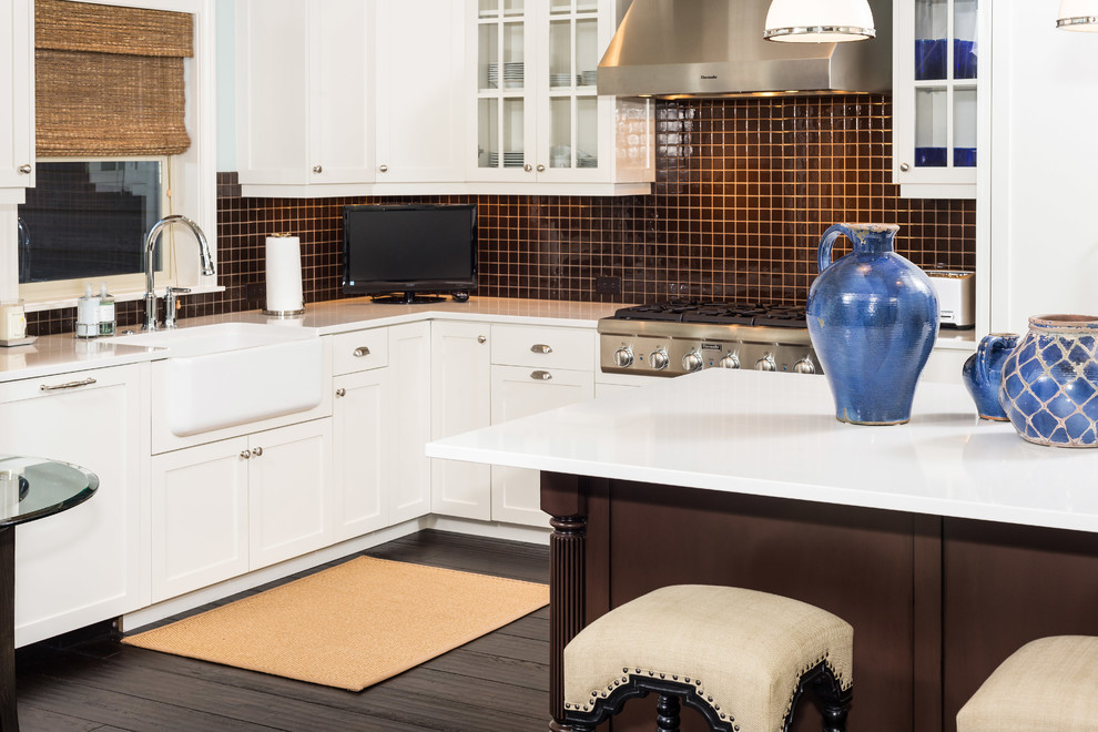 Mid-sized transitional l-shaped dark wood floor and brown floor enclosed kitchen photo with a farmhouse sink, shaker cabinets, white cabinets, quartzite countertops, brown backsplash, mosaic tile backsplash, stainless steel appliances, an island and white countertops