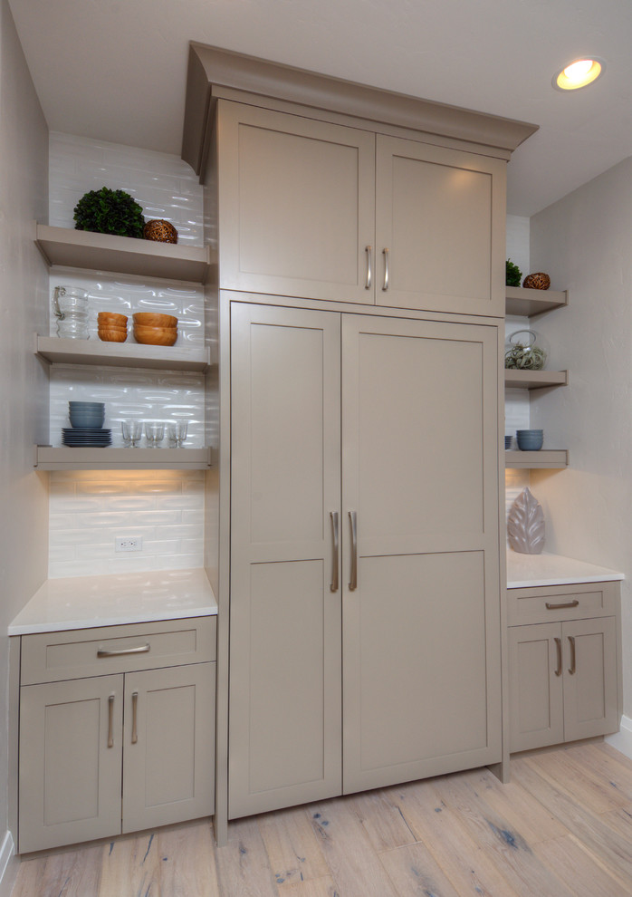 This is an example of a large contemporary single-wall kitchen pantry in Denver with shaker cabinets, grey cabinets, white splashback and light hardwood floors.