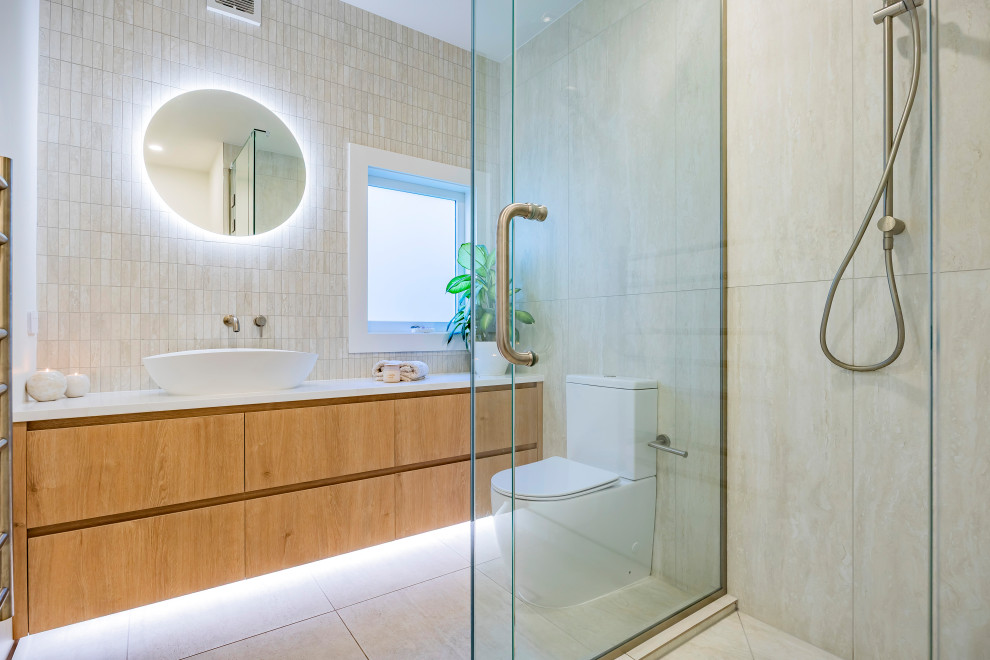 This is an example of a Small contemporary bathroom in Auckland With Flat-panel Cabinets, Medium Wood Cabinets, a Corner Shower, a One-piece Toilet, Multi-coloured Tile, Porcelain Tile, Beige Walls, Porcelain Floors, a Vessel Sink, Engineered Quartz Benchtops, Beige Floor, a Hinged Shower Door, White Benchtops, a Niche, a Single Vanity and a Built-in Vanity.