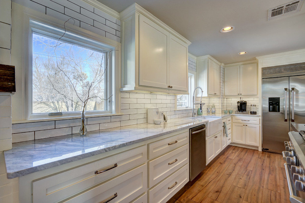Large transitional open plan kitchen in Oklahoma City with a farmhouse sink, shaker cabinets, white cabinets, white splashback, subway tile splashback, stainless steel appliances, medium hardwood floors and multiple islands.