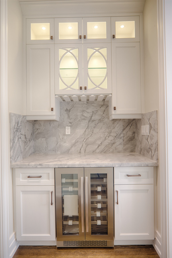 This is an example of a small contemporary single-wall wet bar in Toronto with no sink, recessed-panel cabinets, white cabinets, marble benchtops, grey splashback, marble splashback, dark hardwood floors, brown floor and grey benchtop.