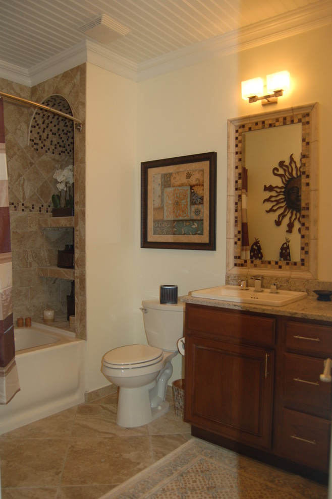 Design ideas for a mid-sized beach style bathroom in New York with a drop-in sink, raised-panel cabinets, brown cabinets, granite benchtops, an alcove tub, a shower/bathtub combo, a one-piece toilet, beige tile, ceramic tile, beige walls and ceramic floors.
