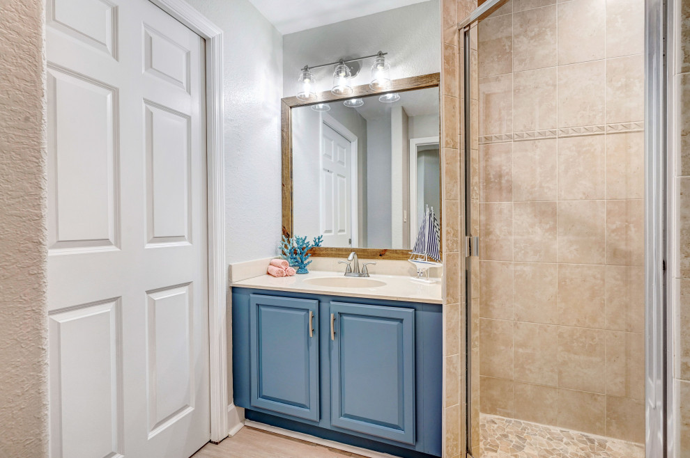 На фото: ванная комната среднего размера в морском стиле с фасадами с выступающей филенкой, синими фасадами, угловым душем, раздельным унитазом, бежевой плиткой, керамической плиткой, серыми стенами, полом из ламината, душевой кабиной, монолитной раковиной, мраморной столешницей, серым полом, душем с распашными дверями, бежевой столешницей, тумбой под одну раковину и встроенной тумбой