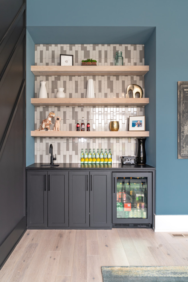 This is an example of a contemporary single-wall wet bar in Nashville with an undermount sink, shaker cabinets, grey cabinets, multi-coloured splashback, light hardwood floors, beige floor and black benchtop.