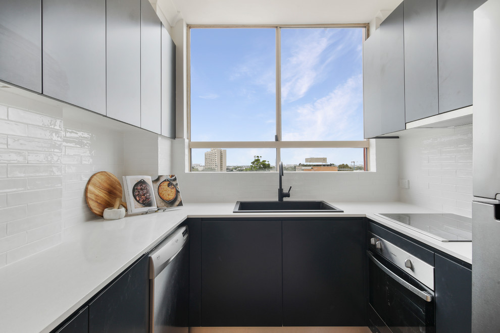 Inspiration for a contemporary u-shaped kitchen in Other with a drop-in sink, flat-panel cabinets, black cabinets, white splashback, stainless steel appliances and white benchtop.