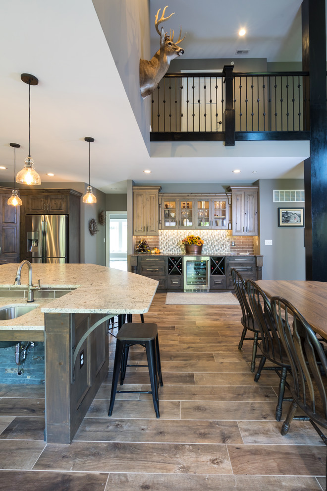 Large country l-shaped open plan kitchen in Philadelphia with a farmhouse sink, raised-panel cabinets, distressed cabinets, quartz benchtops, grey splashback, cement tile splashback, stainless steel appliances, porcelain floors, with island and brown floor.