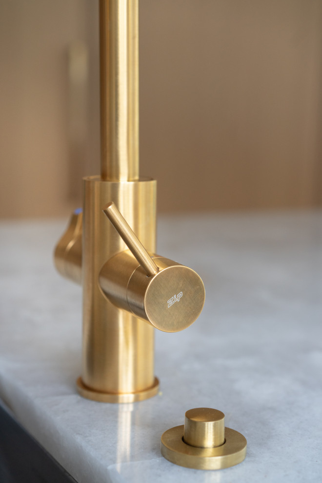 An elegant and modern kitchen faucet with a gold finish, placed near a large win