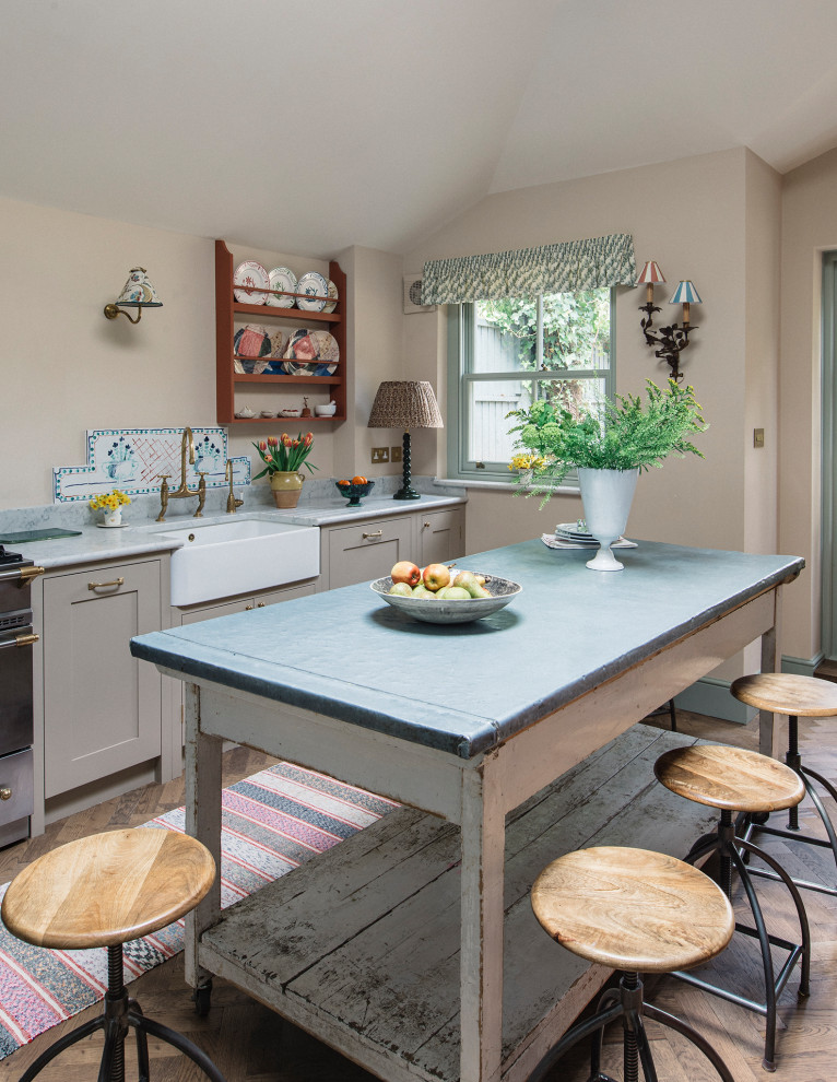 Foto på ett mellanstort vintage grå linjärt kök och matrum, med en rustik diskho, skåp i shakerstil, beige skåp, bänkskiva i kvartsit, beige stänkskydd, svarta vitvaror, en köksö och brunt golv