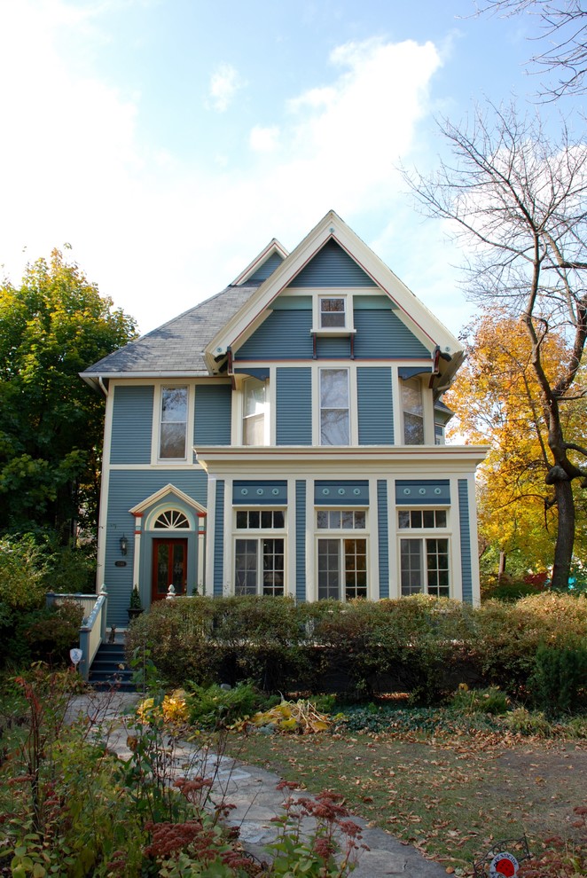 This is an example of a large traditional three-storey blue house exterior in Other with wood siding, a gable roof and a shingle roof.