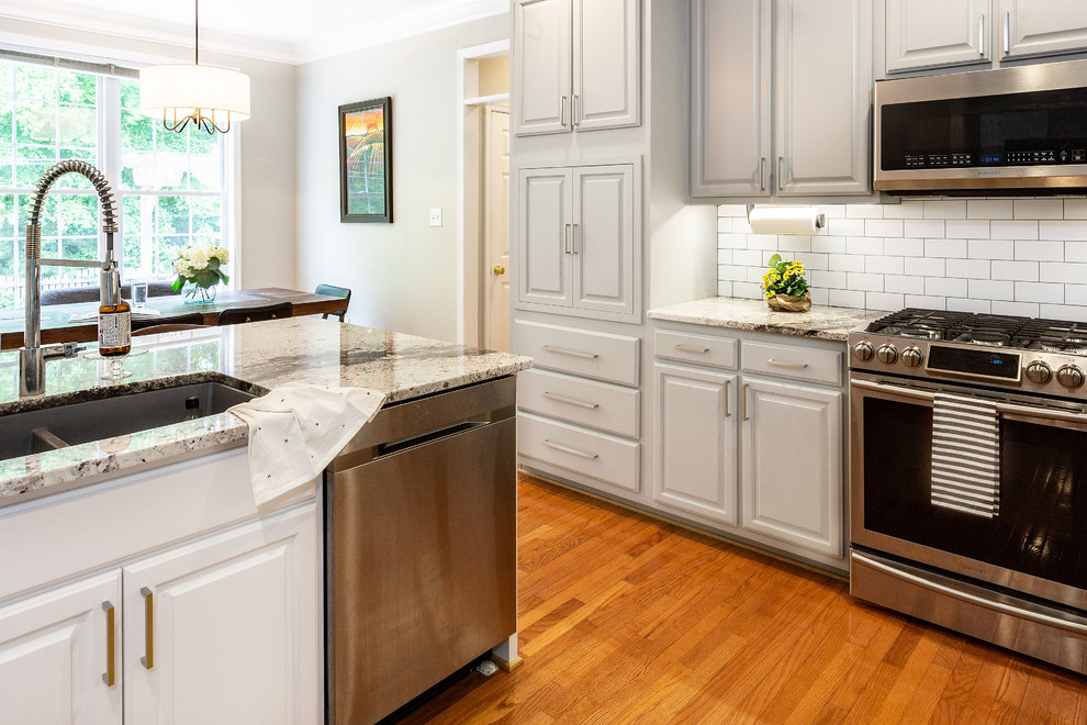 Inspiration for a mid-sized l-shaped medium tone wood floor eat-in kitchen remodel in Richmond with a farmhouse sink, gray cabinets, granite countertops, white backsplash, ceramic backsplash, stainless steel appliances, an island and white countertops