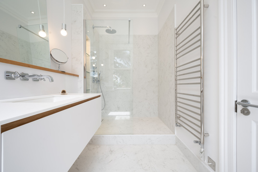 Design ideas for a mid-sized contemporary master bathroom in London with flat-panel cabinets, white cabinets, a wall-mount toilet, white walls, an undermount sink, an open shower, white benchtops, a single vanity, a built-in vanity, an open shower, white tile, marble, marble floors, engineered quartz benchtops and white floor.