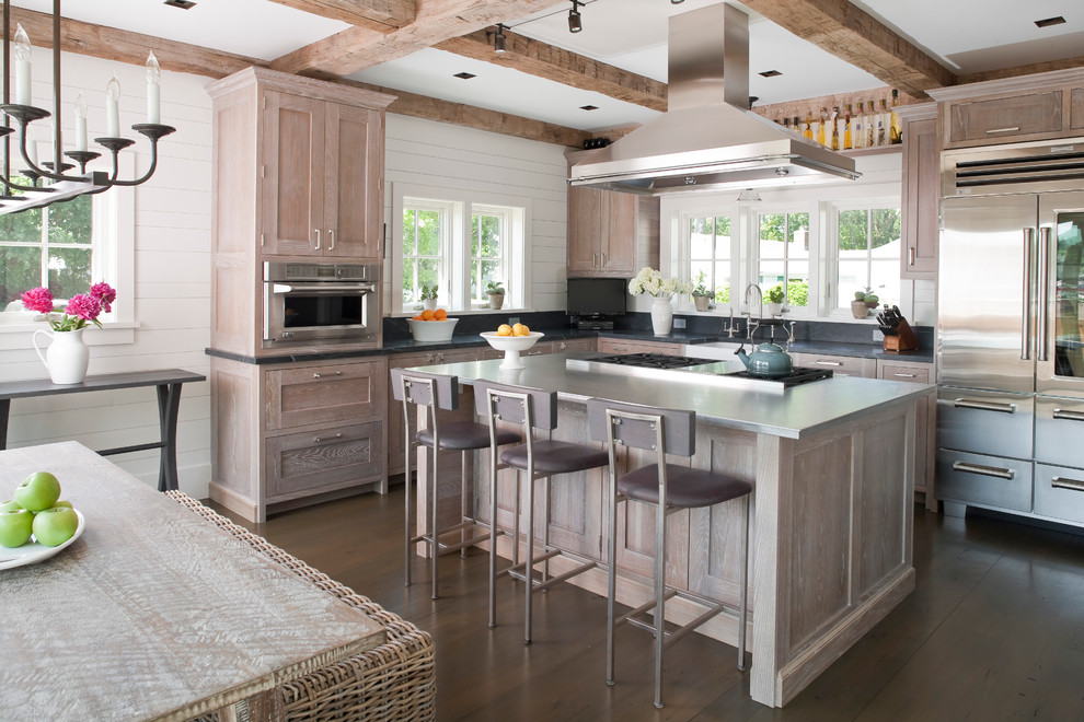 Inspiration for a large beach style l-shaped eat-in kitchen in Bridgeport with a farmhouse sink, recessed-panel cabinets, distressed cabinets, stainless steel benchtops, stainless steel appliances, grey splashback, dark hardwood floors and with island.
