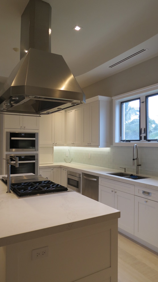 Inspiration for a large transitional l-shaped light wood floor and beige floor enclosed kitchen remodel with a double-bowl sink, shaker cabinets, white cabinets, marble countertops, blue backsplash, glass tile backsplash, stainless steel appliances and an island