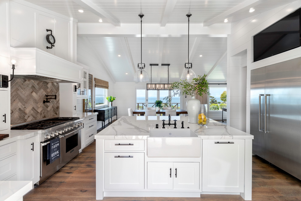 Inspiration for a mid-sized country u-shaped eat-in kitchen in Orange County with a farmhouse sink, shaker cabinets, white cabinets, stainless steel appliances, medium hardwood floors, with island, brown floor, white benchtop, marble benchtops, white splashback and timber splashback.
