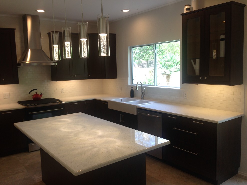 Large transitional u-shaped porcelain tile and brown floor enclosed kitchen photo in Austin with a farmhouse sink, recessed-panel cabinets, dark wood cabinets, limestone countertops, white backsplash, subway tile backsplash, stainless steel appliances, an island and white countertops