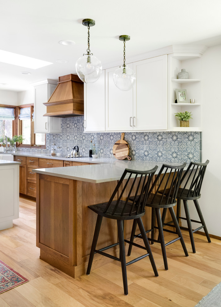 Mid-sized country u-shaped eat-in kitchen in Seattle with a farmhouse sink, shaker cabinets, white cabinets, quartz benchtops, multi-coloured splashback, ceramic splashback, stainless steel appliances, light hardwood floors, with island, brown floor and grey benchtop.