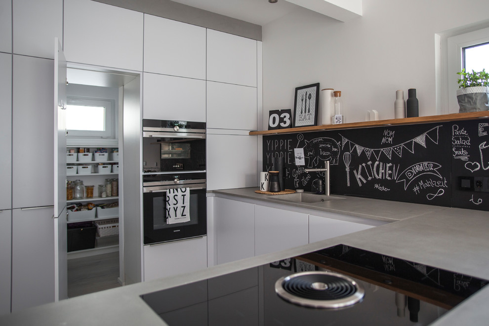 Diseño de cocina escandinava de tamaño medio abierta con fregadero integrado, puertas de armario blancas, encimera de cemento y electrodomésticos de acero inoxidable