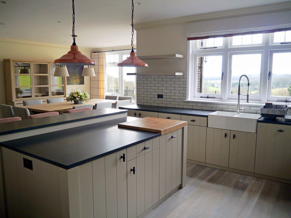 Inspiration for a contemporary kitchen in London with a farmhouse sink, recessed-panel cabinets, granite benchtops, subway tile splashback, stainless steel appliances, medium hardwood floors and with island.