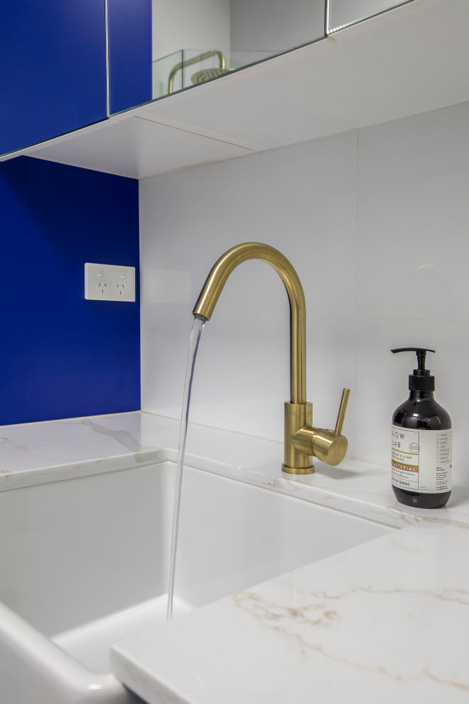 This is an example of a mid-sized transitional galley laundry room in Sydney with a farmhouse sink, shaker cabinets, blue cabinets, quartz benchtops and white benchtop.