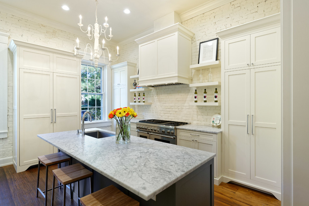 Inspiration for a traditional kitchen in Cincinnati with an undermount sink, shaker cabinets, white cabinets, white splashback, brick splashback, dark hardwood floors, with island, brown floor, grey benchtop, marble benchtops and panelled appliances.
