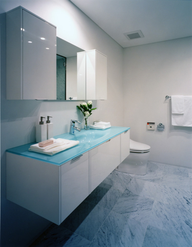 На фото: маленький туалет в стиле модернизм с плоскими фасадами, синими фасадами, унитазом-моноблоком, белыми стенами, мраморным полом, монолитной раковиной, стеклянной столешницей, белым полом, синей столешницей, встроенной тумбой, потолком с обоями и обоями на стенах для на участке и в саду с