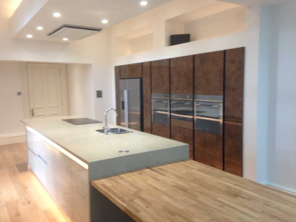 This is an example of a large contemporary galley open plan kitchen in Edinburgh with flat-panel cabinets, with island, an undermount sink, concrete benchtops and light hardwood floors.