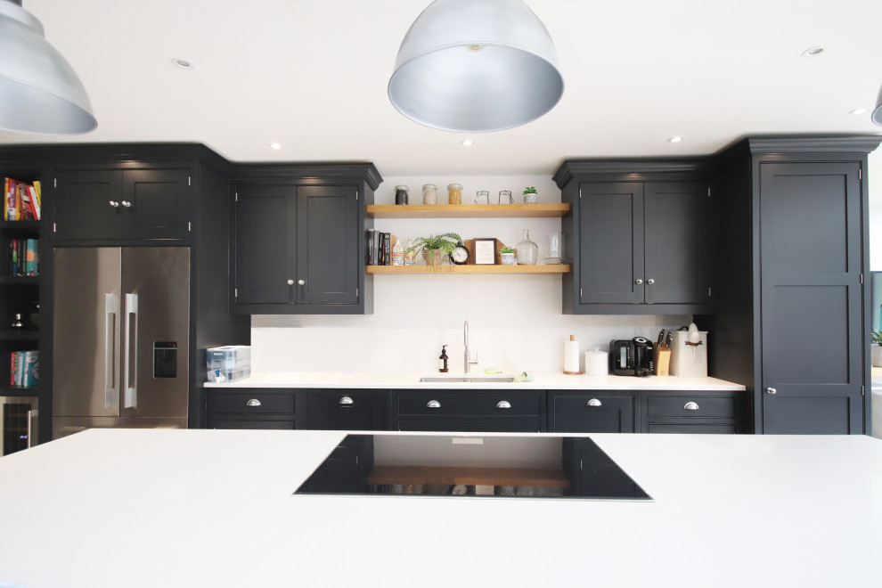 Inspiration for a large modern cream and black l-shaped open plan kitchen in Cambridgeshire with a built-in sink, shaker cabinets, black cabinets, composite countertops, white splashback, granite splashback, stainless steel appliances, limestone flooring, an island, beige floors and white worktops.