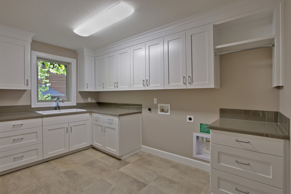 Inspiration for a large contemporary l-shaped dedicated laundry room with a single-bowl sink, shaker cabinets, white cabinets, tile benchtops, beige walls, ceramic floors and a side-by-side washer and dryer.