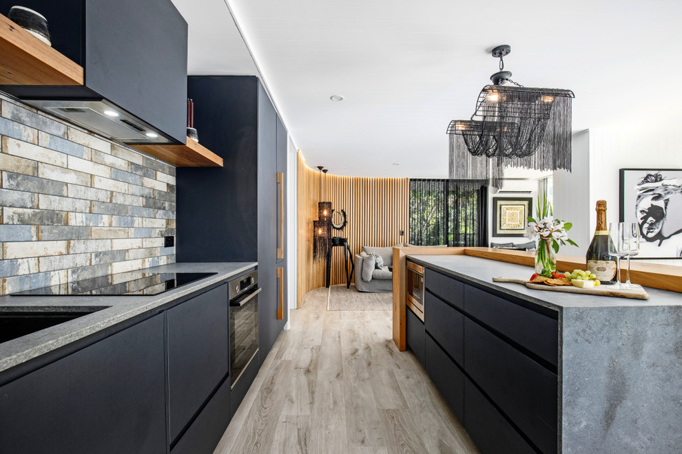 Design ideas for a small beach style single-wall open plan kitchen in Sunshine Coast with an undermount sink, flat-panel cabinets, grey cabinets, concrete benchtops, multi-coloured splashback, ceramic splashback, black appliances, ceramic floors, with island, grey floor and brown benchtop.