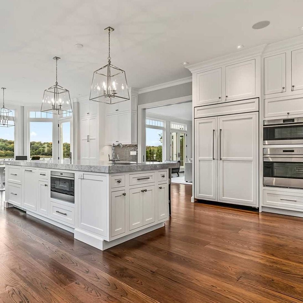 Inspiration for a large transitional l-shaped dark wood floor and brown floor open concept kitchen remodel with beaded inset cabinets, white cabinets, granite countertops, gray backsplash, glass tile backsplash, stainless steel appliances, an island and gray countertops