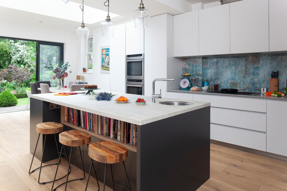 Mid-sized contemporary eat-in kitchen in London with an undermount sink, flat-panel cabinets, white cabinets, blue splashback, medium hardwood floors, with island, brown floor, grey benchtop, marble benchtops, metal splashback and stainless steel appliances.