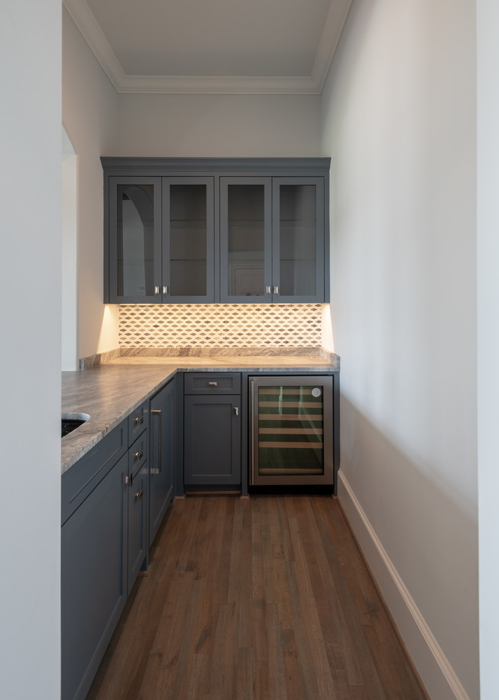 This is an example of a mid-sized transitional l-shaped wet bar in Dallas with an undermount sink, shaker cabinets, blue cabinets, granite benchtops, grey splashback, mosaic tile splashback, medium hardwood floors, brown floor and grey benchtop.