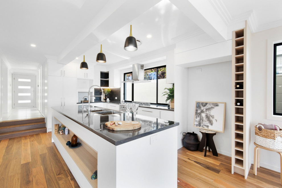 This is an example of a mid-sized modern l-shaped open plan kitchen in Brisbane with a double-bowl sink, white cabinets, laminate benchtops, window splashback, stainless steel appliances, medium hardwood floors, with island, multi-coloured floor and black benchtop.