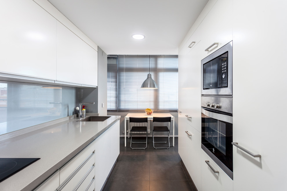 Design ideas for a large contemporary galley separate kitchen in Valencia with an undermount sink, flat-panel cabinets, white cabinets, stainless steel appliances, no island, grey floor, grey benchtop, grey splashback and glass sheet splashback.