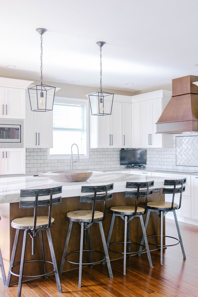Eat-in kitchen - mid-sized transitional l-shaped medium tone wood floor and brown floor eat-in kitchen idea in Omaha with a farmhouse sink, shaker cabinets, white cabinets, quartzite countertops, white backsplash, subway tile backsplash, stainless steel appliances, an island and white countertops